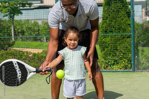 Black father teaching daughter to play paddle tennis 