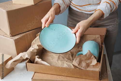 woman packs handmade plates into boxes. small business and entrepreneurship. a business woman sends an order for delivery. online store selling tableware and home decor. kraft cardboard box