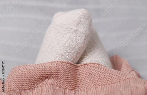 Women's feet in knitted woolen white socks at home under a plaid. Selective focus.