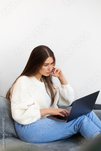 An attractive brunette is sitting at home on the couch and using a laptop. Online training. 