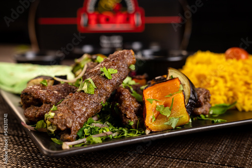 Traditional middle east kefta or kofta kebab of a mix of ground beef and lamb meat grilled on skewers served on a skillet with roasted garlic and onion on a table of barn wood, close-up photo