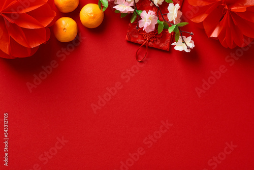 Chinese New Year 2023 year of the rabbit. Red packet envelope, flowers, mandarins, festival decorations on red background. Flat lay, top view.
