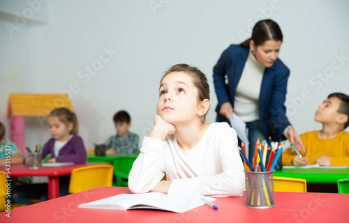 Portrait of tired schoolgirl sitting at pupils desk at lesson in primary school