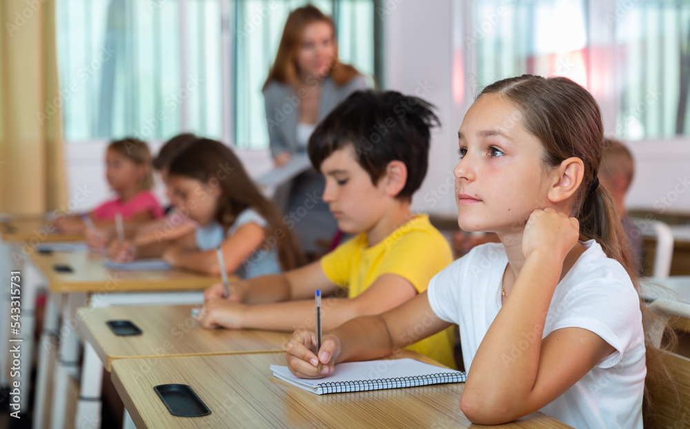 Fototapeta premium Schoolgirl sitting in classroom during lesson in elementary school. High quality photo