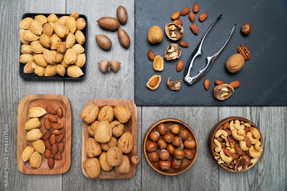 nuts in bowls and a nutcracker on a gray table. top view, Assortment of nuts - cashew, hazelnuts, almonds, walnuts, pistachio, pecans, pine nuts, peanut. nuts in bowls and a nutcracker on a gray table. top view, Assortment of nuts - cashew, hazelnuts, almonds, walnuts, pistachio, pecans, pine nuts, peanut.