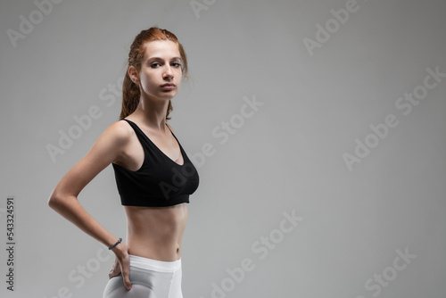 Фотография Fit girl with black top and white leggings posing against gray background