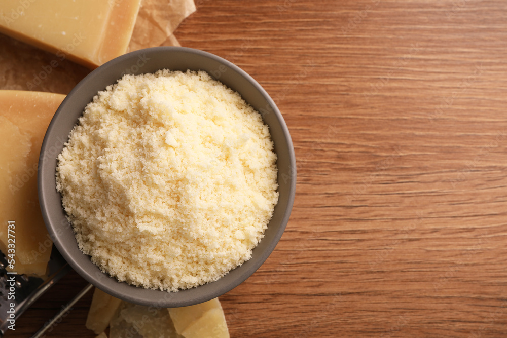 Delicious grated parmesan cheese in bowl on wooden table, flat lay. Space for text Delicious grated parmesan cheese in bowl on wooden table, flat lay. Space for text