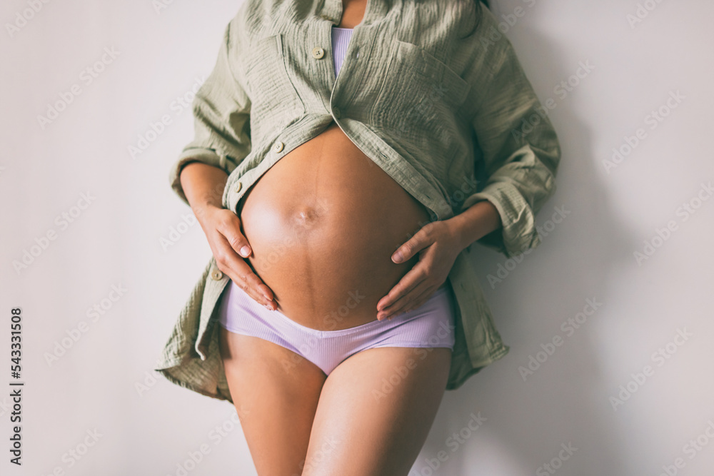 Pregnancy belly closeup. Pregnant woman wearing underwear and casual cotton  shirt at home relaxing holding expecting tummy for skincare, health,  lifestyle Photos