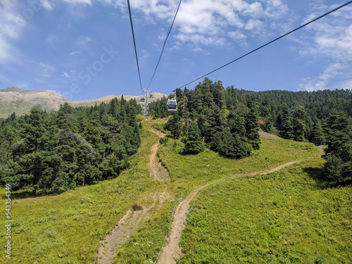 Arkhyz, Karachay-Cherkessia, Russia - August 21, 2022: View of the cable car with cabins in the resort area of Arkhyz against the backdrop of the Caucasian mountains and coniferous forest