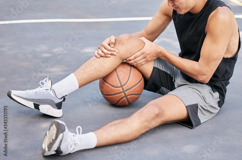 Basketball, man and knee in sports injury on the court holding painful, sore or tender area in the outdoors. Basketball player suffering from leg pain, joint or inflammation in sport match or game photo