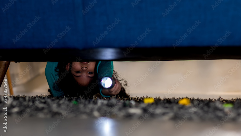 Girl with a flashlight looking under the bed. evening night time. kid ...