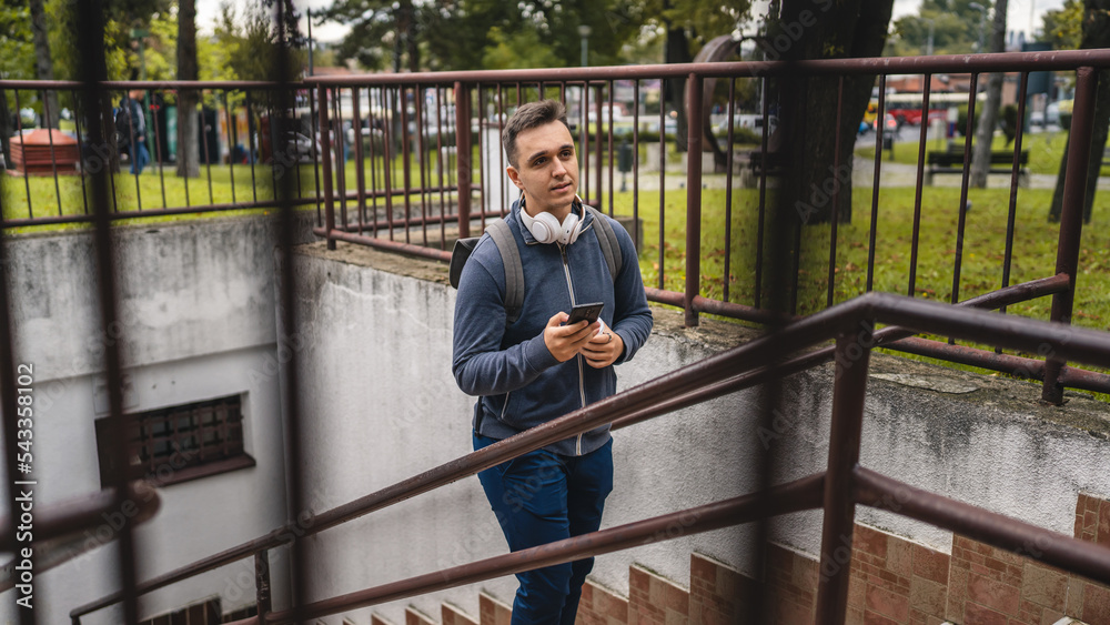 One man young adult male walking up the stairs steps in the city in day with cup of coffee and mobile phone real people tourist or student copy space One man young adult male walking up the stairs steps in the city in day with cup of coffee and mobile phone real people tourist or student copy space