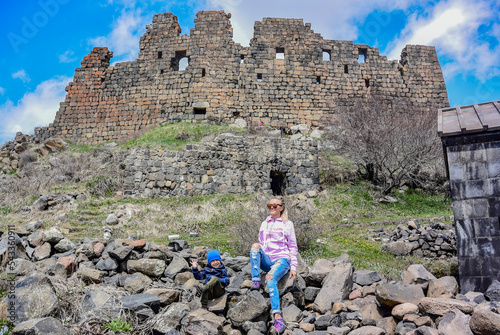 A girl with a child on the background of the 7th-century Amberd fortress, located on the slopes of mount Aragats at the confluence of the Arkashen and Amberd rivers, may 3, 2019, Armenia. photo