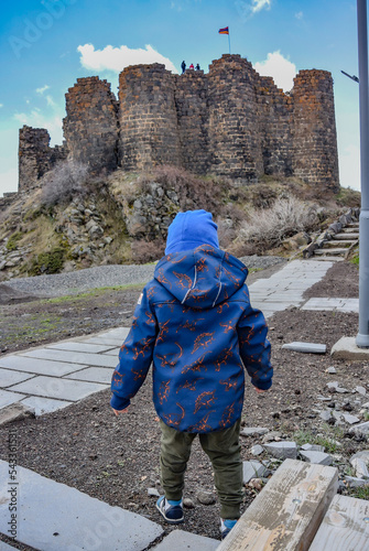 A small boy on the background of the 7th-century Amberd fortress, located on the slopes of mount Aragats at the confluence of the Arkashen and Amberd rivers, may 3, 2019, Armenia. photo