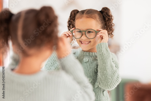 Children, mirror and girl with glasses at optometry store, testing or shopping for new eyewear. Vision, choice and happy kid trying spectacles or lenses at optics shop while looking at reflection.