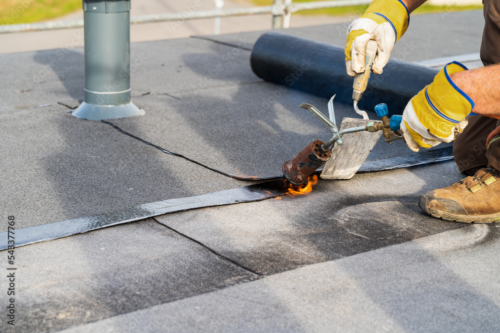 Man Heating and melting bitumen roofing Flat roof installation.