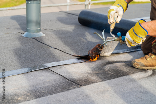 Man Heating and melting bitumen roofing Flat roof installation.