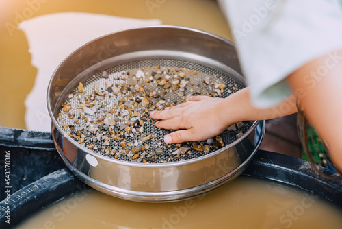 Fototapeta Child hand picking pebbles at the sieve at archaeological excavations or extraction of gold and other gems at the prospecting site