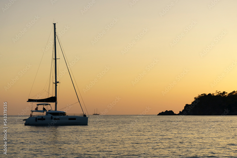 Sunset with a yacht on the tropical mediterranean sea. Evening or morning landscape with beautiful orange sun, calm water and soft light in summer