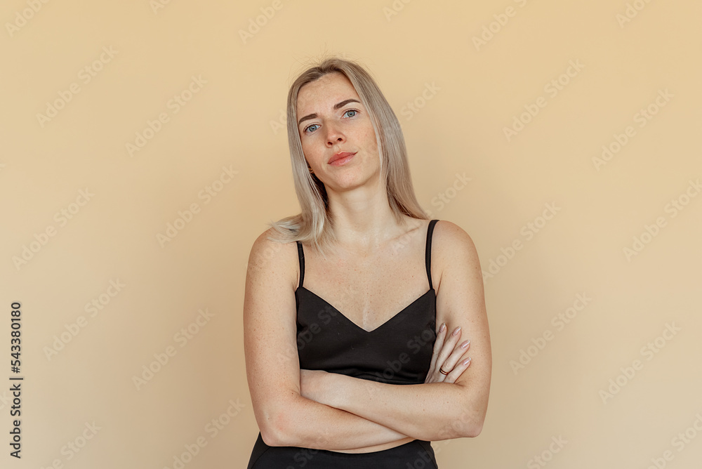 Serious young woman with freckles cross arms on chest, looking confident and professional, standing over beige background Serious young woman with freckles cross arms on chest, looking confident and professional, standing over beige background