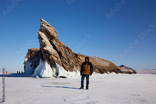 A man traveler stands at the Dragon Rock on Ogoy Island. A cape popular with tourists, covered with icicles. Frozen Lake Baikal. Winter trip. 