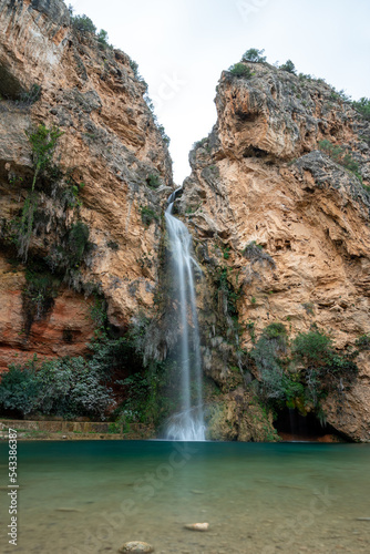 Beautiful long exposure vertical landscape of a waterfall in the cave de turches surrounded by vegetation and rocks in Buñol, Valencia, Spain