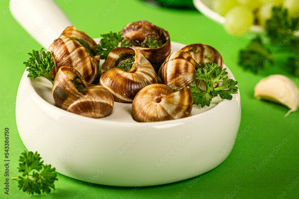 Close up of Baked Bourgogne Escargot Snails with garlic herbs butter in ceramics pan on green background Close up of Baked Bourgogne Escargot Snails with garlic herbs butter in ceramics pan on green background