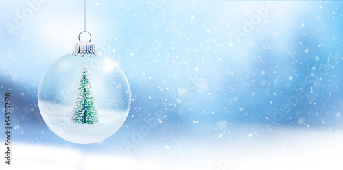 Gläserne Weihnachtskugel mit Tannenbaum vor unscharfem Hintergrund