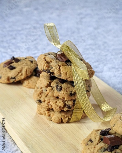 Chocolate chips cookies wrapped on golden ribbon on the wooden board with the blurry background