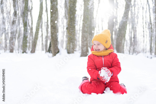 Cute little girl in pink snowsuit plays with snow in winter forest photo