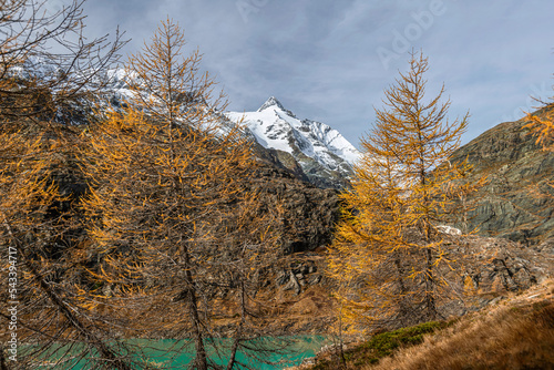 Margaritze artifical lake with Grossglockner Summit in Hohe Tauern in Alps with glowing larch trees in autumn, Austria photo