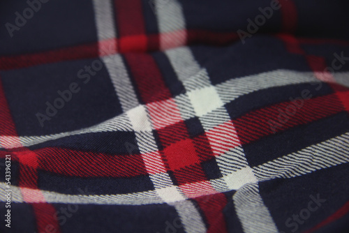 Close up textured soft drapery fabric garment or clothing. Square lines dark black checkered pattern with white and red decorations. Classic clothes pattern.