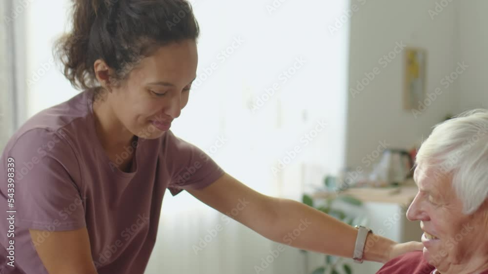 Young woman holding hand of senior man in wheelchair and talking with him at home Young woman holding hand of senior man in wheelchair and talking with him at home