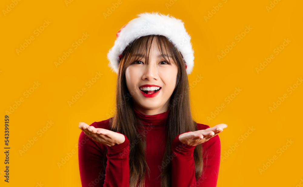 Merry Christmas. Young asian smiling woman in red long sleeve t shirt wearing santa hat hands pointing and giving yellow background. Merry Christmas. Young asian smiling woman in red long sleeve t shirt wearing santa hat hands pointing and giving yellow background.