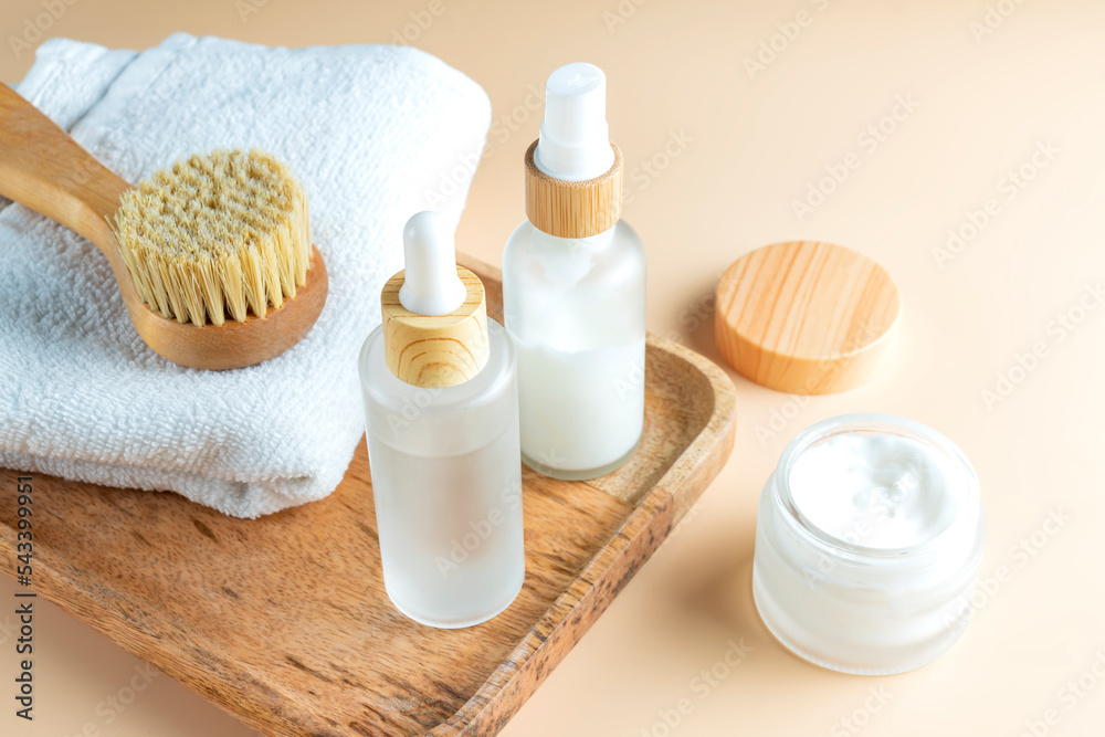 skin exfolation and rejuvination concept. Drop bottle with fruit peeling, face mask and face massaging brush with natural bristle on wooden tray on beige background with copy space. skin exfolation and rejuvination concept. Drop bottle with fruit peeling, face mask and face massaging brush with natural bristle on wooden tray on beige background with copy space.
