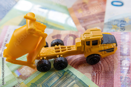 Side view of a toy concrete mixer on the background of different euro banknotes. The concept of expensive modern construction.