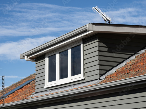View of gray shed roof dormer loft with white window and clay colored tiles