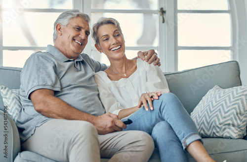 Happy senior couple, hug and watching TV for entertainment, relax or bonding time together at home. Elderly man and woman relaxing on living room sofa with smile for movie, show or media streaming