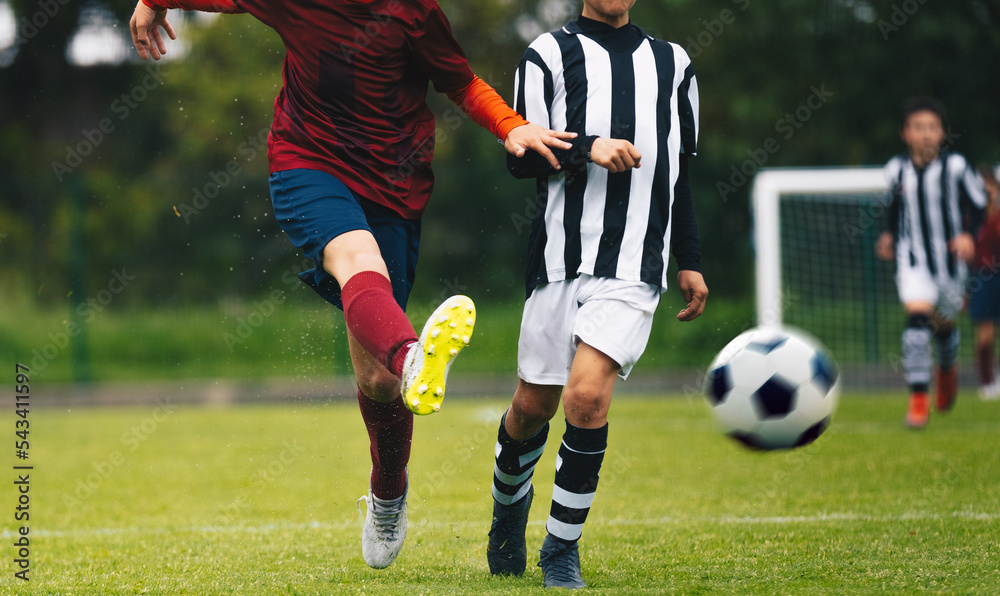 Obraz premium Teenage boys kicking football. Two player in soccer duel on grass pitch. Soccer forward shoot a ball. Defensive player in blurred background