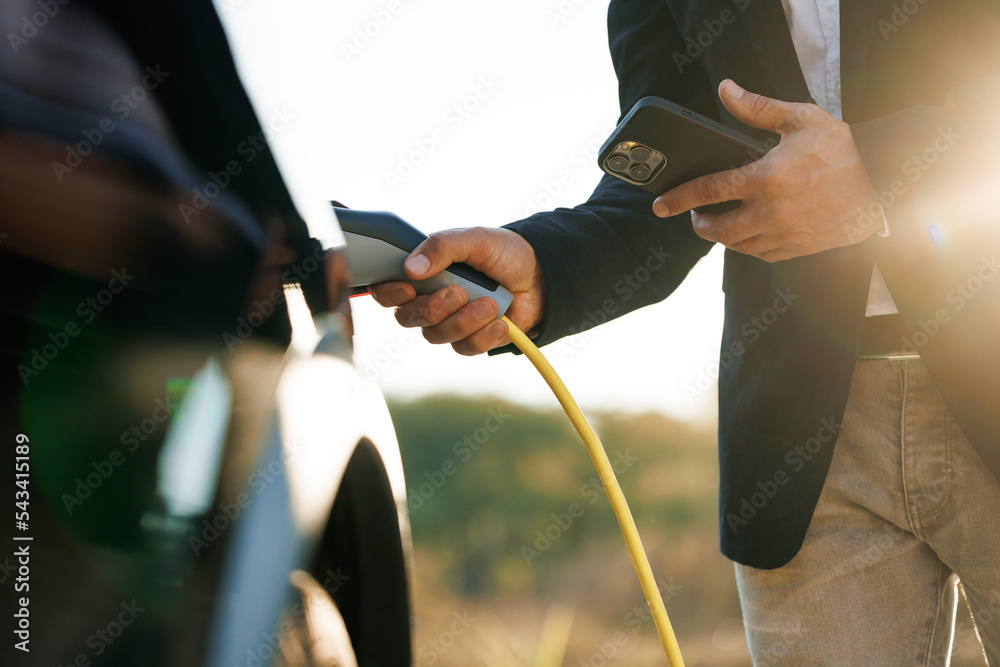 Male charging EV vehicle outdoors at sun light. Businessman unplugging