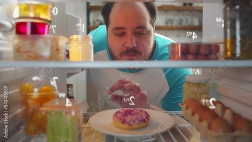 Overweight man on diet look into fridge with calories graphic over products.  photo