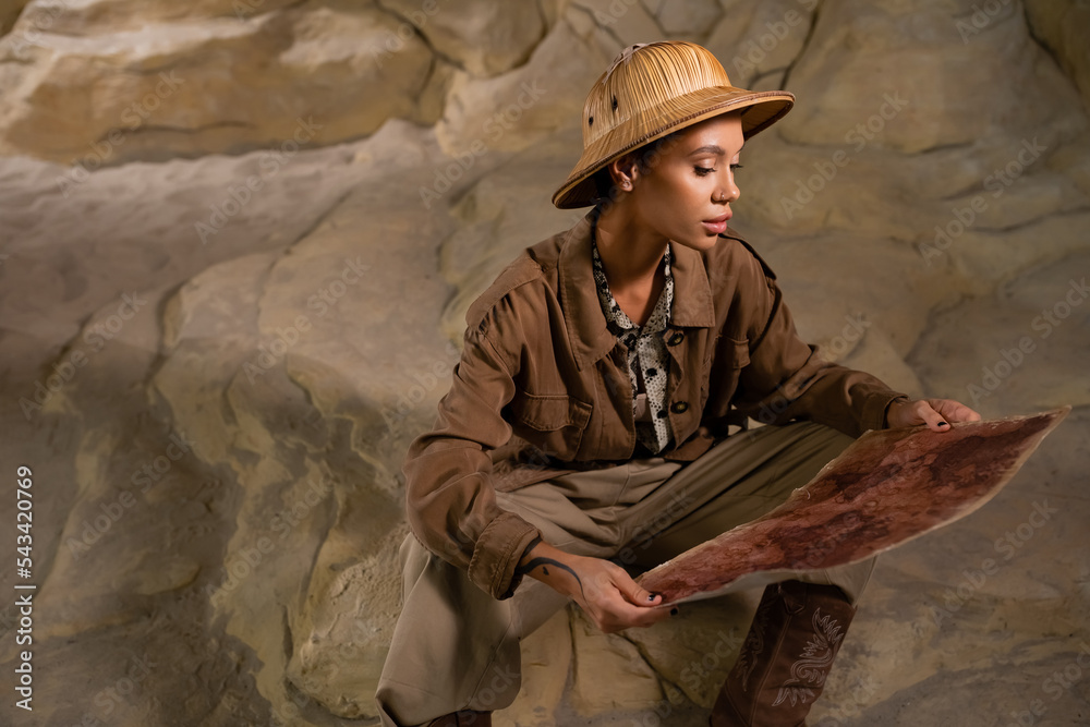 young archaeologist in safari style outfit sitting on rock and looking at  ancient map. Stock Photo | Adobe Stock