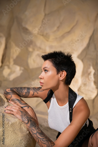 side view of tattooed archaeologist with short hair looking away in cave.