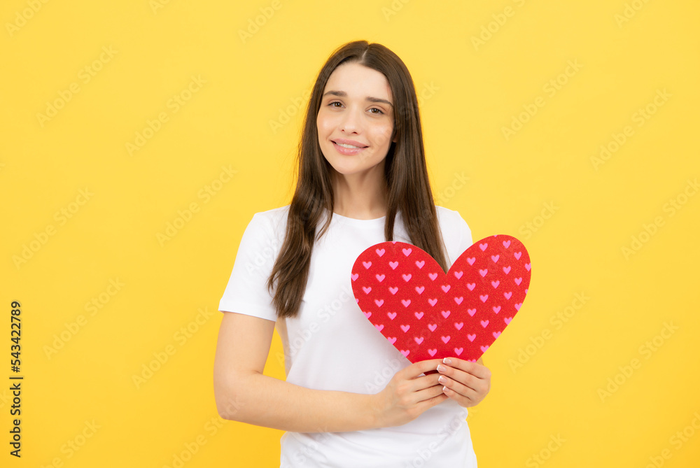 Portrait of pretty smiling woman holding paper heart in her hands on yellow background. Love concept. Portrait of pretty smiling woman holding paper heart in her hands on yellow background. Love concept.