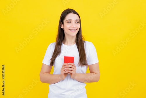 Close-up portrait of attractive dreamy girl holding in hands drinking latte isolated on yellow background. Young brunette woman drinking a cup of coffee.
