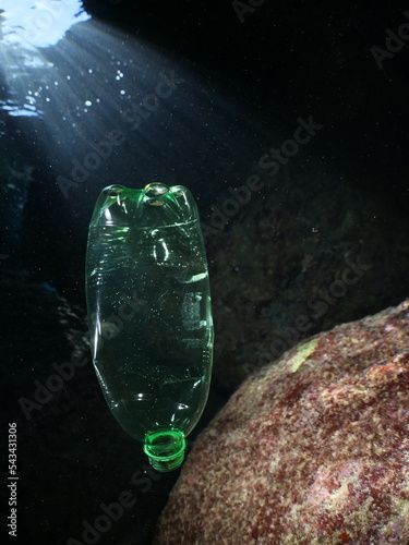 plastic bottle in a cave underwater sun beams and rays ocean pollution