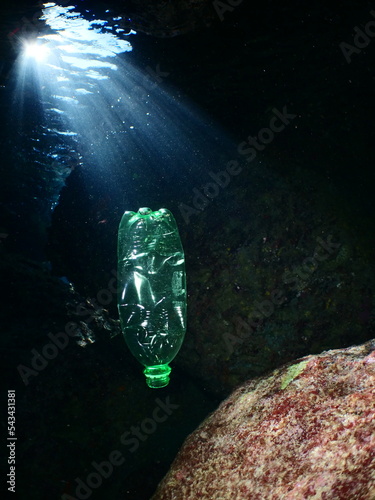 plastic bottle in a cave underwater sun beams and rays ocean pollution