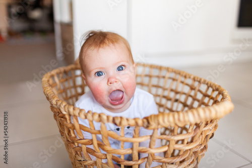 Happy young baby sitting up in washing basket being loud with wide open mouth