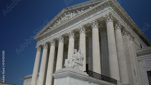 Facade of US Supreme Court building with Authority of Justice sculpture in front in Washington DC on a sunny summer evening.