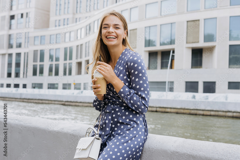 Fototapeta premium Portrait of a happy young woman. The model drinks ice coffee in the summer on the street